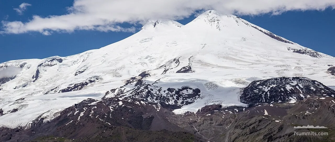Snow-capped twin peaks of Mount Elbrus seen from Mount Cheget under blue sky