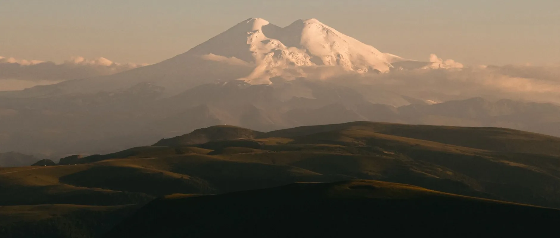 elbrus — Serene view of snow-covered Mount Elbrus with surrounding landscape at dusk.